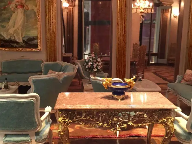 Formal sitting room with pale blue upholstered chairs around a gilded marble-topped table