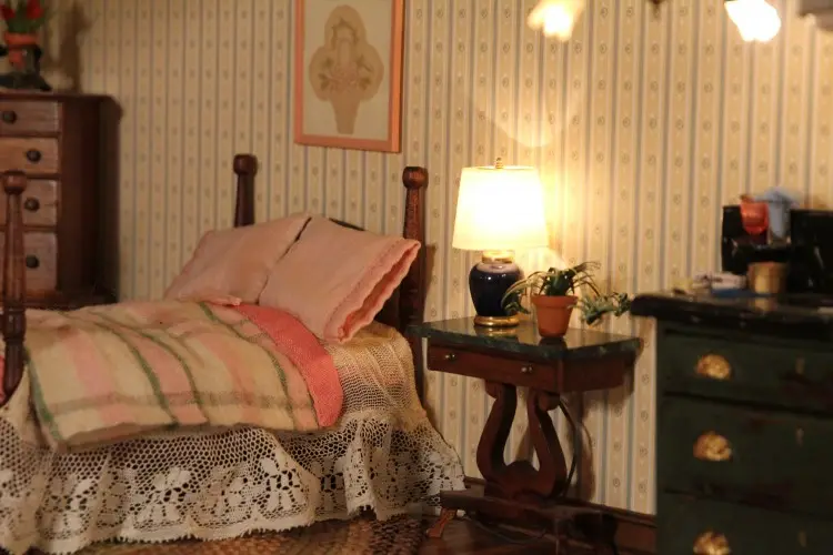 Bedroom with a striped quilt, lace bedskirt and a lamp on a mahogany nightstand