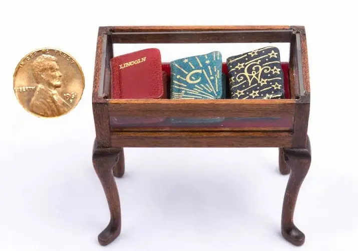 Miniature book stand holding tiny books, beside a penny for scale