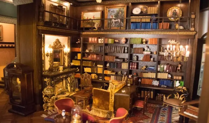 Library with floor-to-ceiling bookshelves, a gilded fireplace and red armchairs